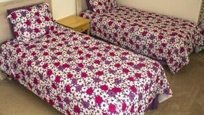 Una habitación con dos camas individuales, cada una con una colcha de estampado floral, una mesita de noche de madera y una pared lisa.