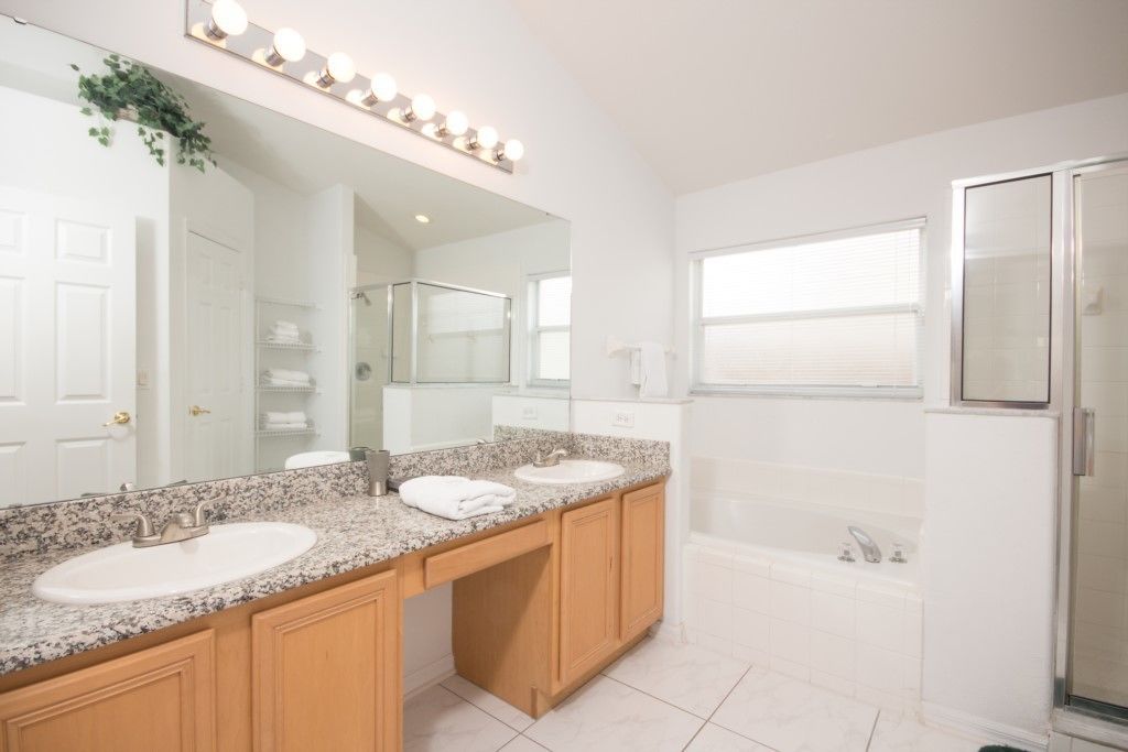 A modern bathroom with two sinks, a large mirror with lights, a shower, and a bathtub.