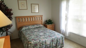 Ein Schlafzimmer mit einem Bett, einem Nachttisch, einer Lampe und einem Fenster mit Jalousien.