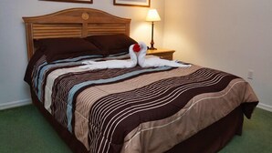 A neatly made bed with a striped bedspread, a wooden headboard, and a lamp on a bedside table.