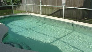 A rectangular swimming pool with clear water, surrounded by a wooden fence and a tiled deck.