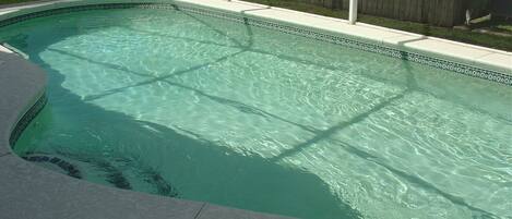 A rectangular swimming pool with clear water, surrounded by a wooden fence and a tiled deck.