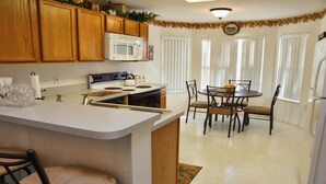 A kitchen with wooden cabinets, a white microwave, a stove, and a dining area with a table and chairs.