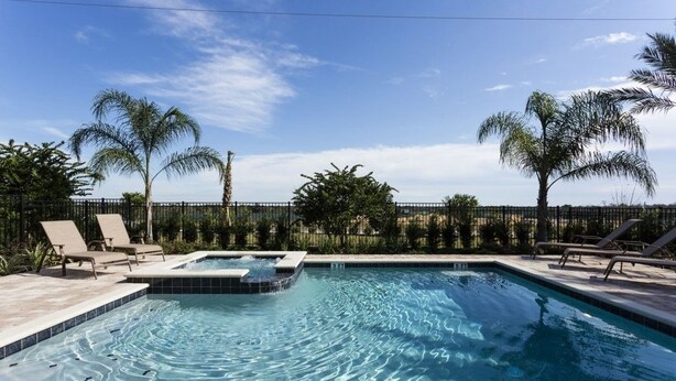 Une piscine rectangulaire avec un jacuzzi, entourée de chaises longues et de palmiers.