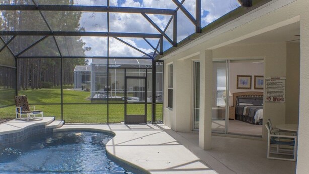 A swimming pool with a glass enclosure, a lawn, and a bedroom with a bed and a chair. - Ip60121 - Highlands Reserve - 4 Bed 2 Baths Villa (Davenport)