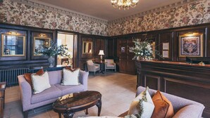 Een klassieke hotel lobby met een bank, fauteuils, een salontafel en een receptiebalie.