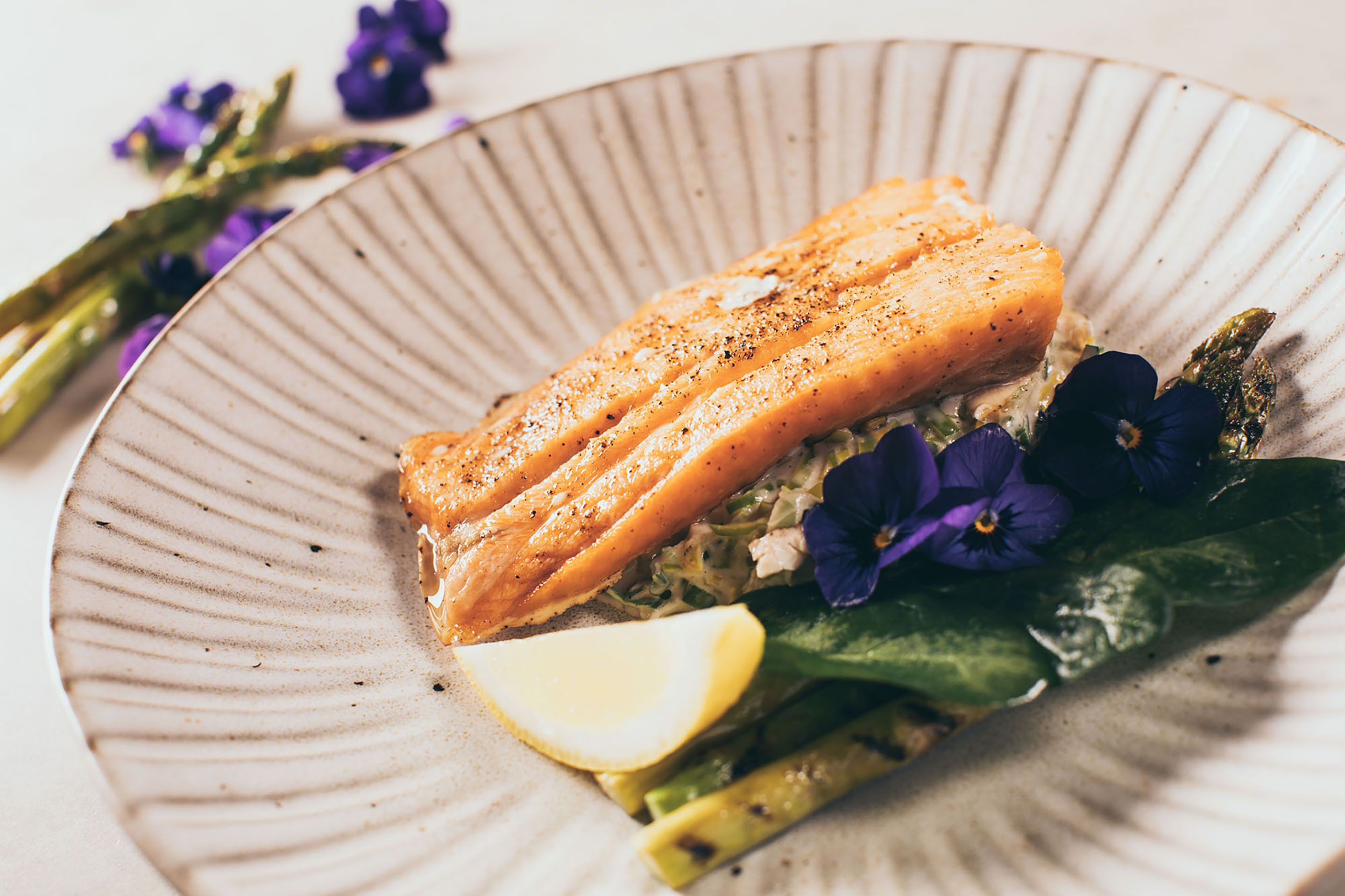 Un plato de salmón, espárragos y flores moradas.