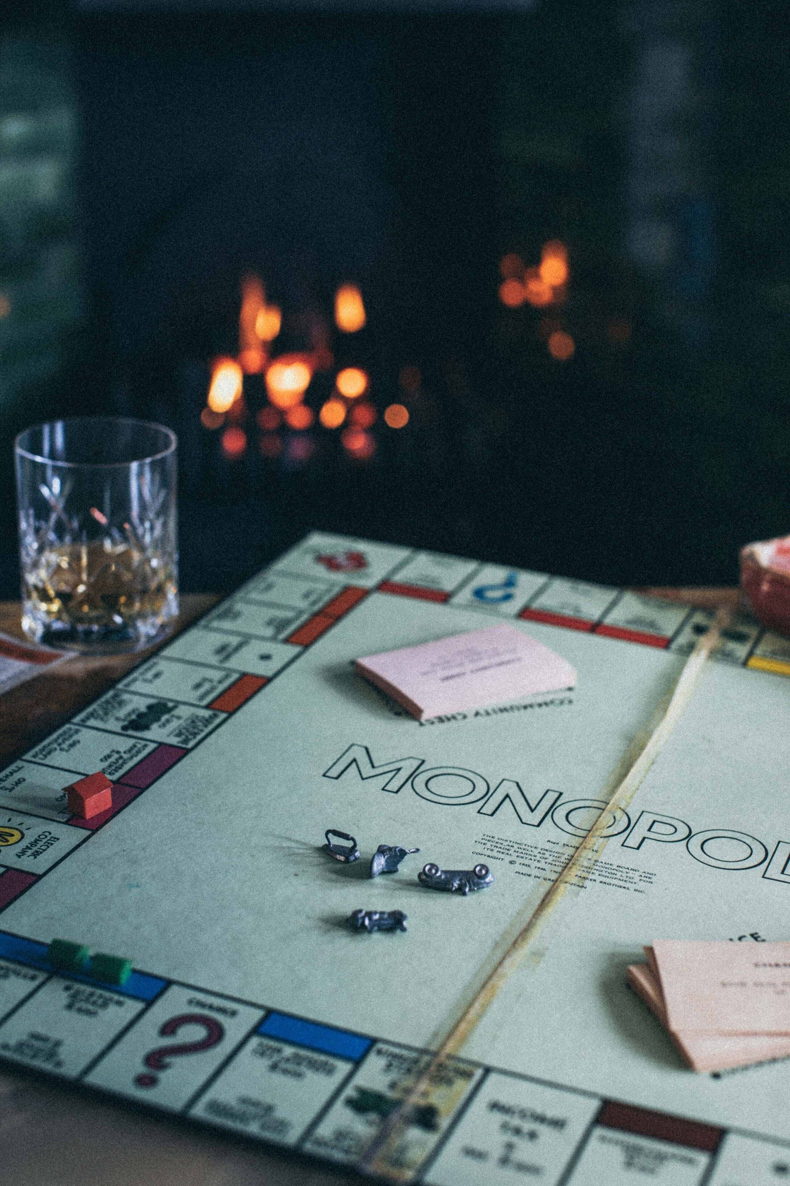A Monopoly board game with tokens and a glass of whiskey on a table.