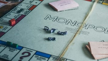 A Monopoly board game with tokens and a glass of whiskey on a table.