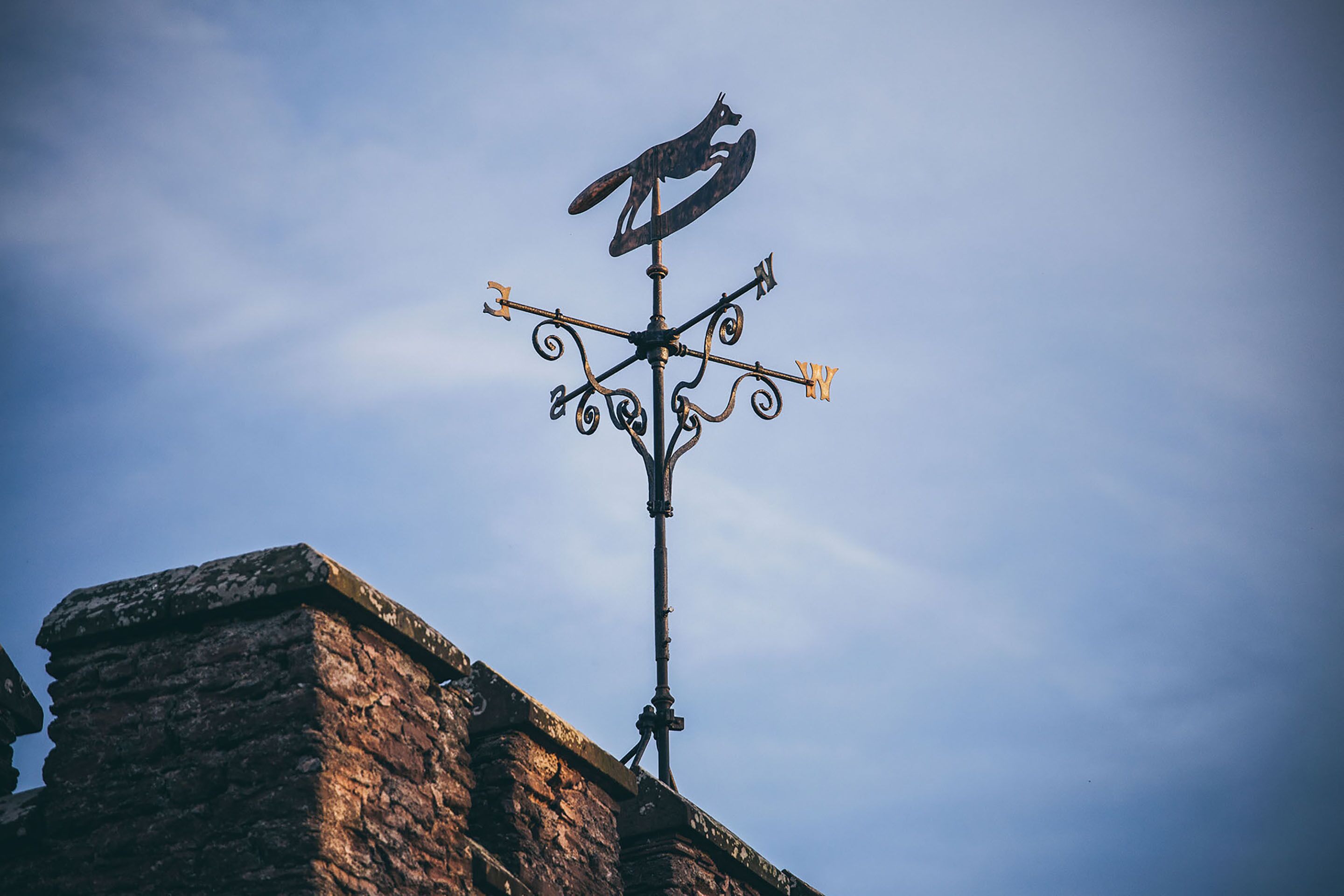 A weather vane with a fox design on a metal pole, mounted on a brick structure.