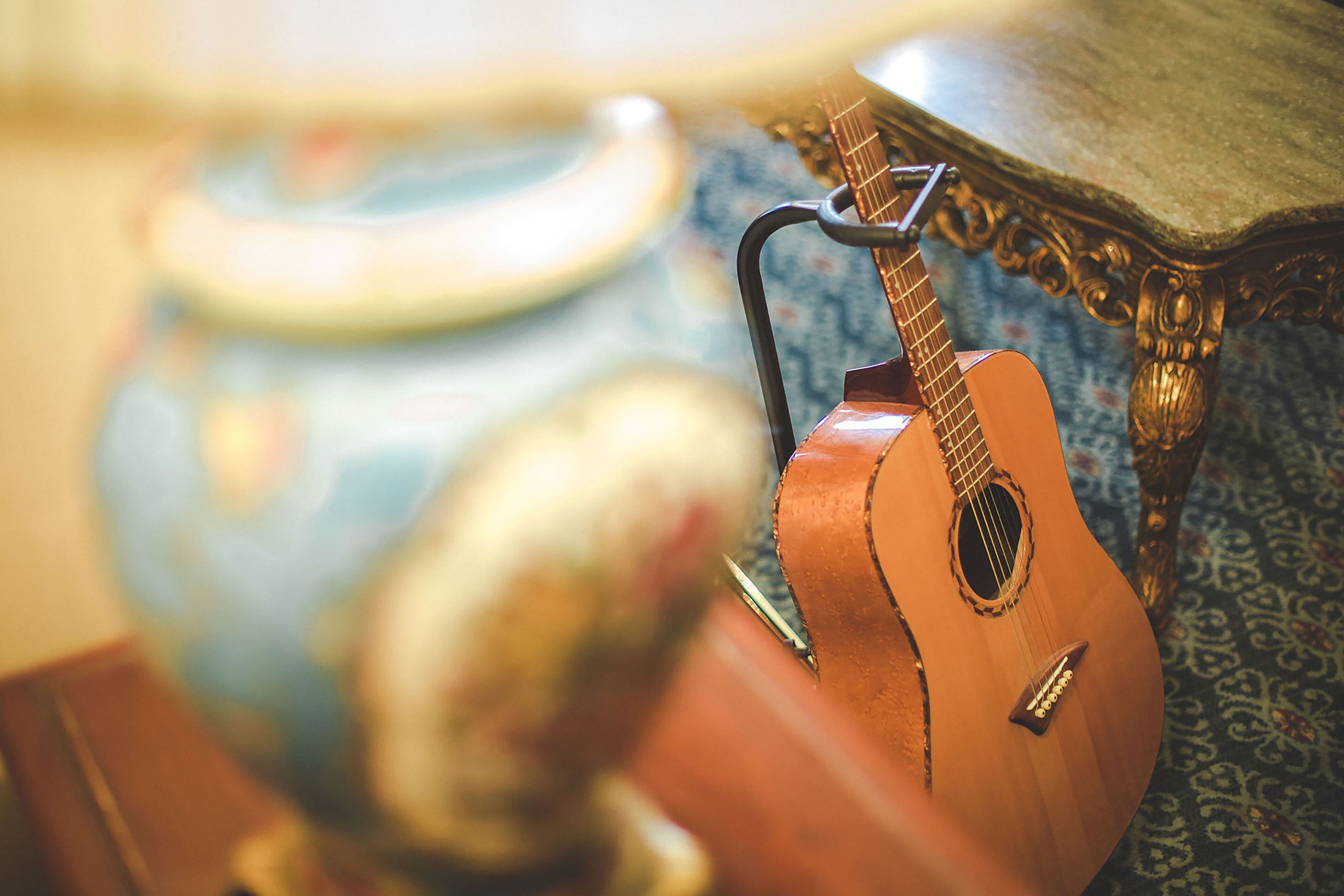 A close-up of a wooden guitar with a pickguard, positioned next to a blue ceramic jug with a handle.