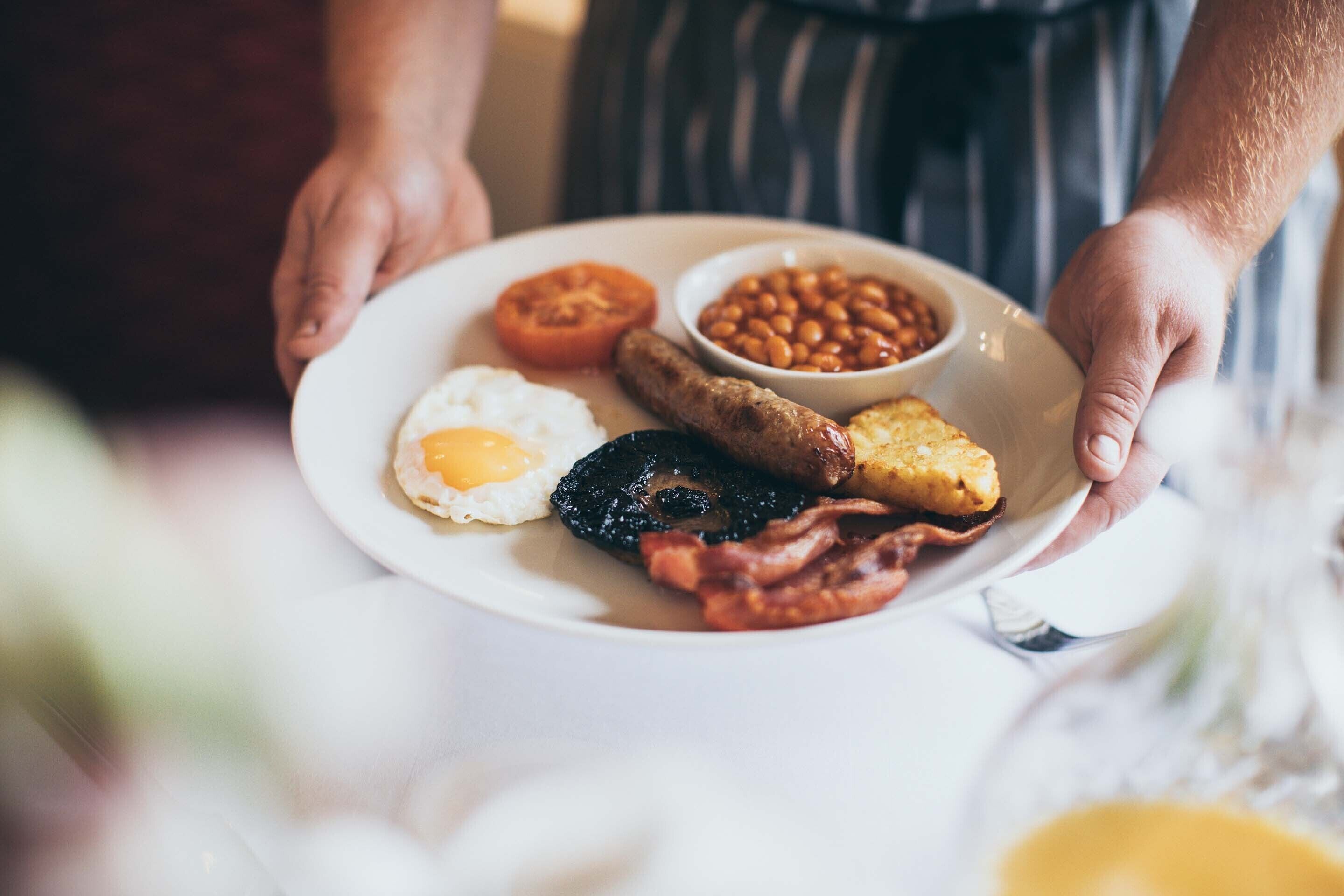 A plate of breakfast food including eggs, beans, sausage, bacon, and toast.