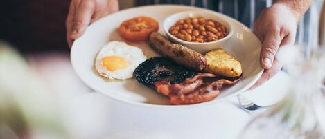 A plate of breakfast food including eggs, beans, sausage, bacon, and toast.