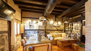 A rustic interior with stone walls, wooden beams, a glass dining table, and a cozy seating area. - El Tomillar CR (Pasaron de la Vera)