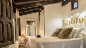 A bedroom with a large bed, a wooden door, a white wall, and a ceiling with exposed beams. - El Tomillar CR (Pasaron de la Vera)
