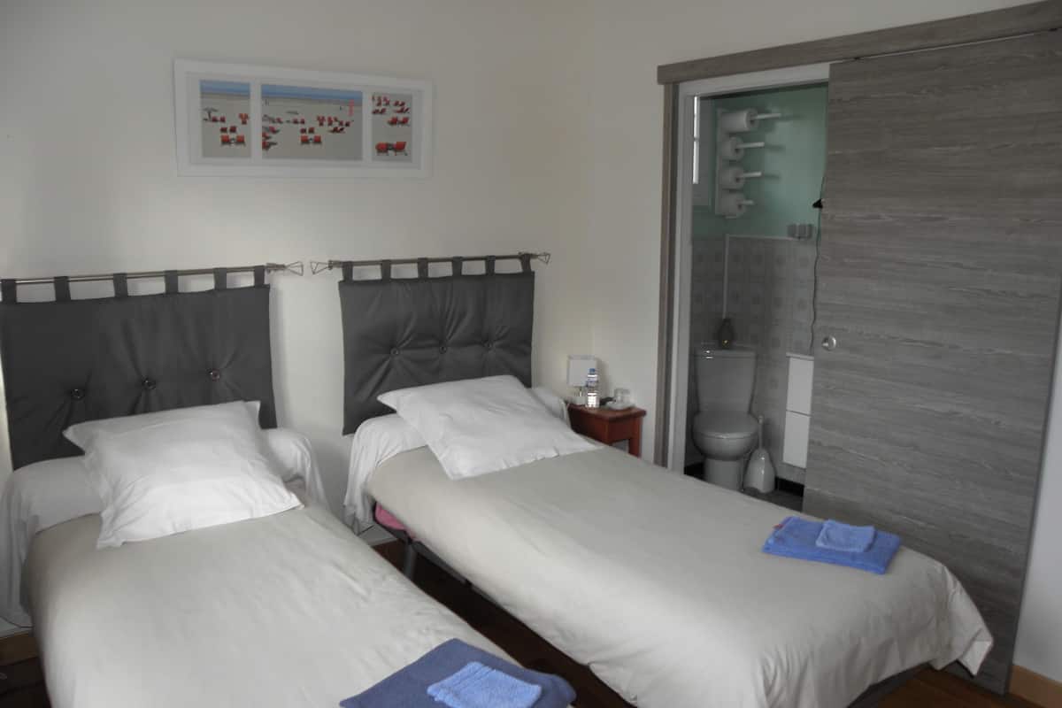 A hotel room with two beds, a small bedside table, a framed picture on the wall, and a bathroom visible through an open door.