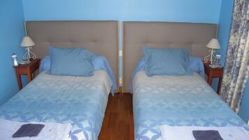 A double room with two beds, each with a headboard, a bedside table, a lamp, and a water bottle.