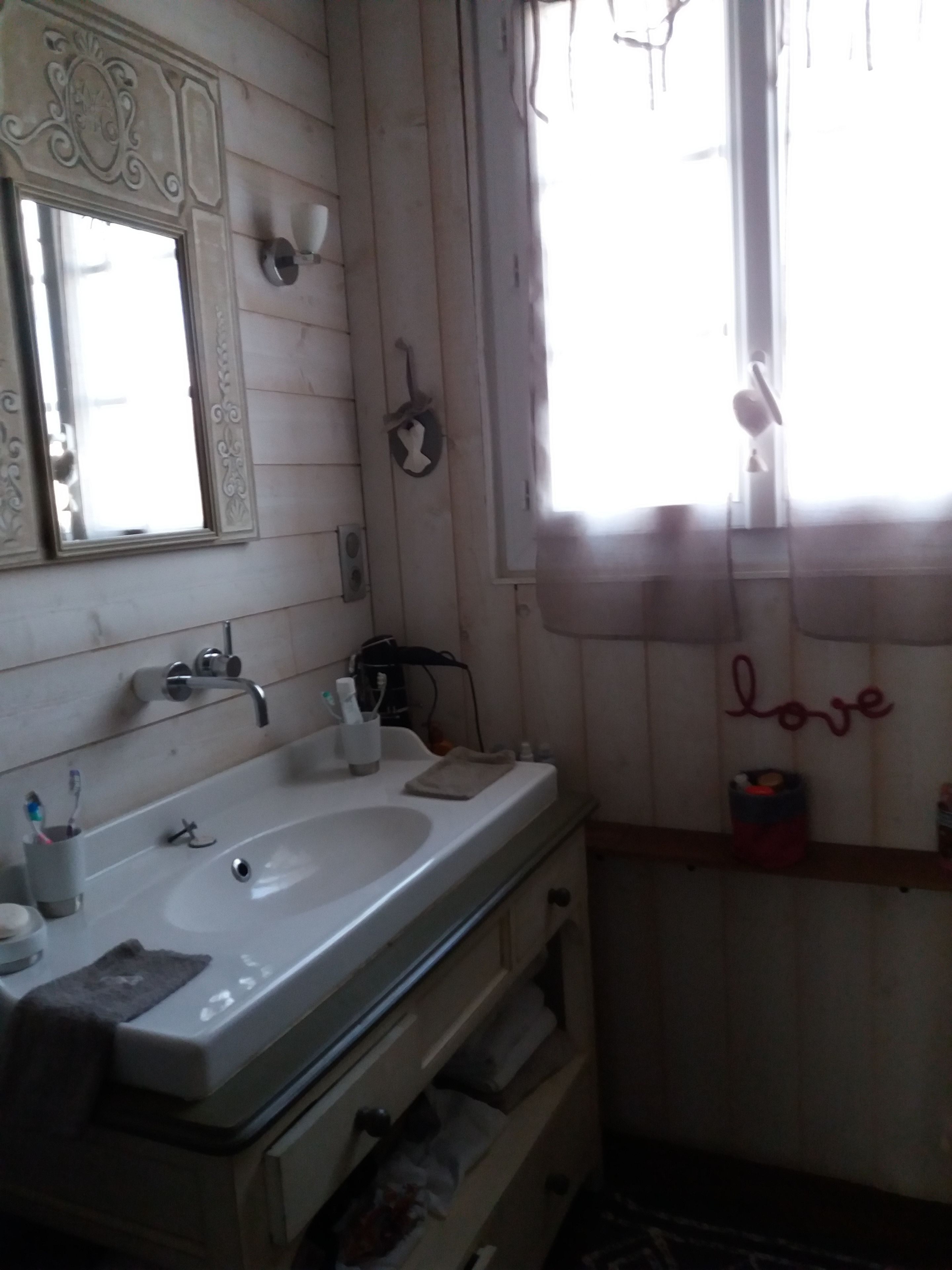 A bathroom with a double sink, a mirror with ornate detailing, a towel rack, and a 'love' sign on the wall.