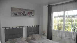 A bedroom with two beds, a nightstand, a lamp, a painting, and a window with curtains. - Chambres d'hôtes La Planche Pinçon (Teloché)