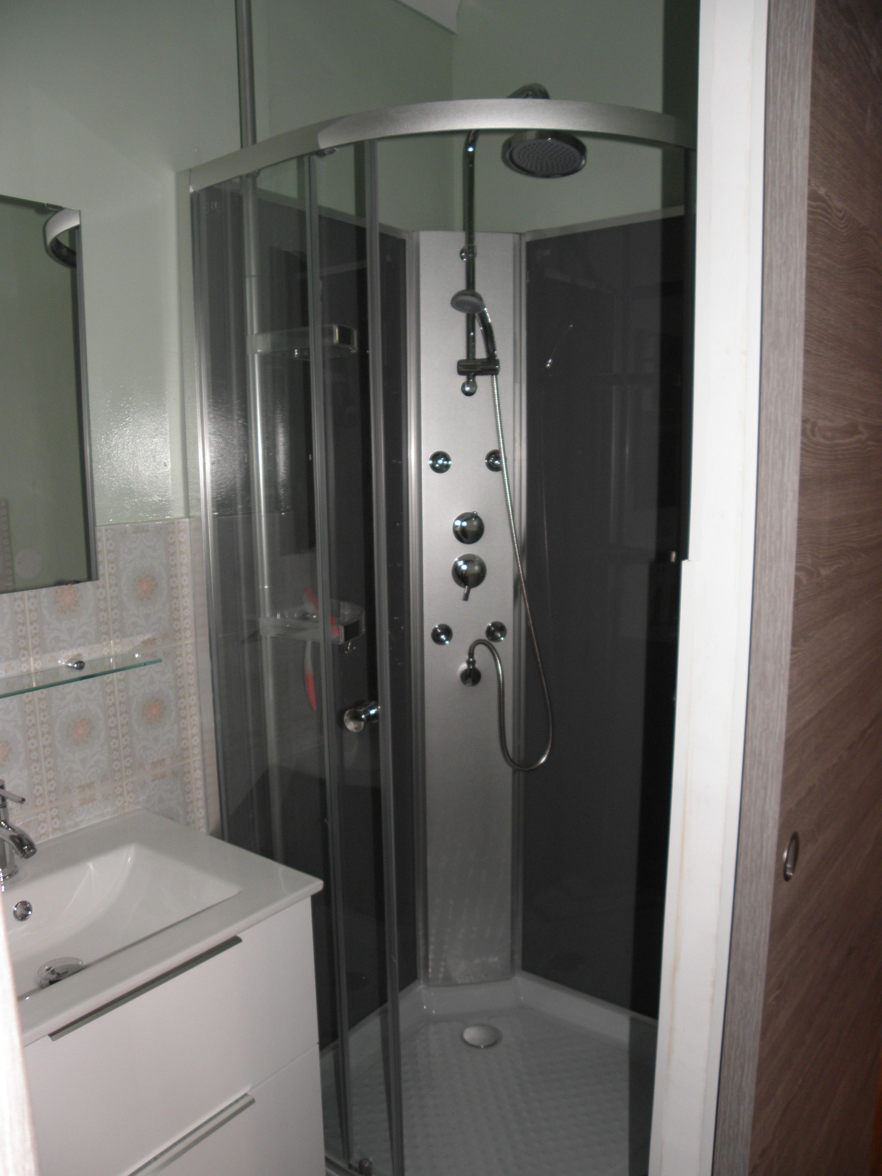 Cabina de ducha con paredes de vidrio, cabezal de ducha manual y llave de pared.