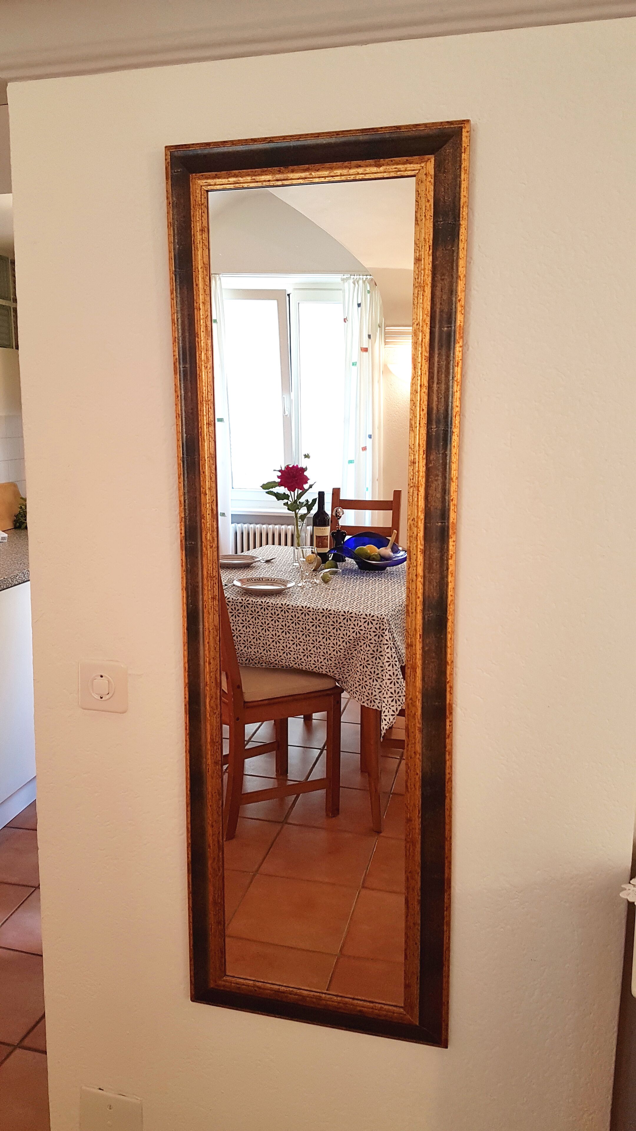A dining area with a table set for two, a chair, a vase with flowers, and a bowl of fruit.