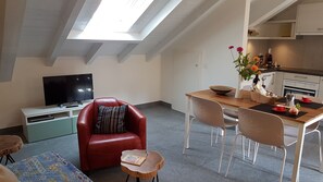 A cozy living room with a red leather chair, a wooden dining table, and a flat-screen TV. - Residenza Motta (Locarno)