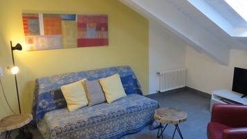 Une pièce chaleureuse avec un canapé à motifs, une petite table ronde, un fauteuil rouge, un téléviseur et un radiateur.