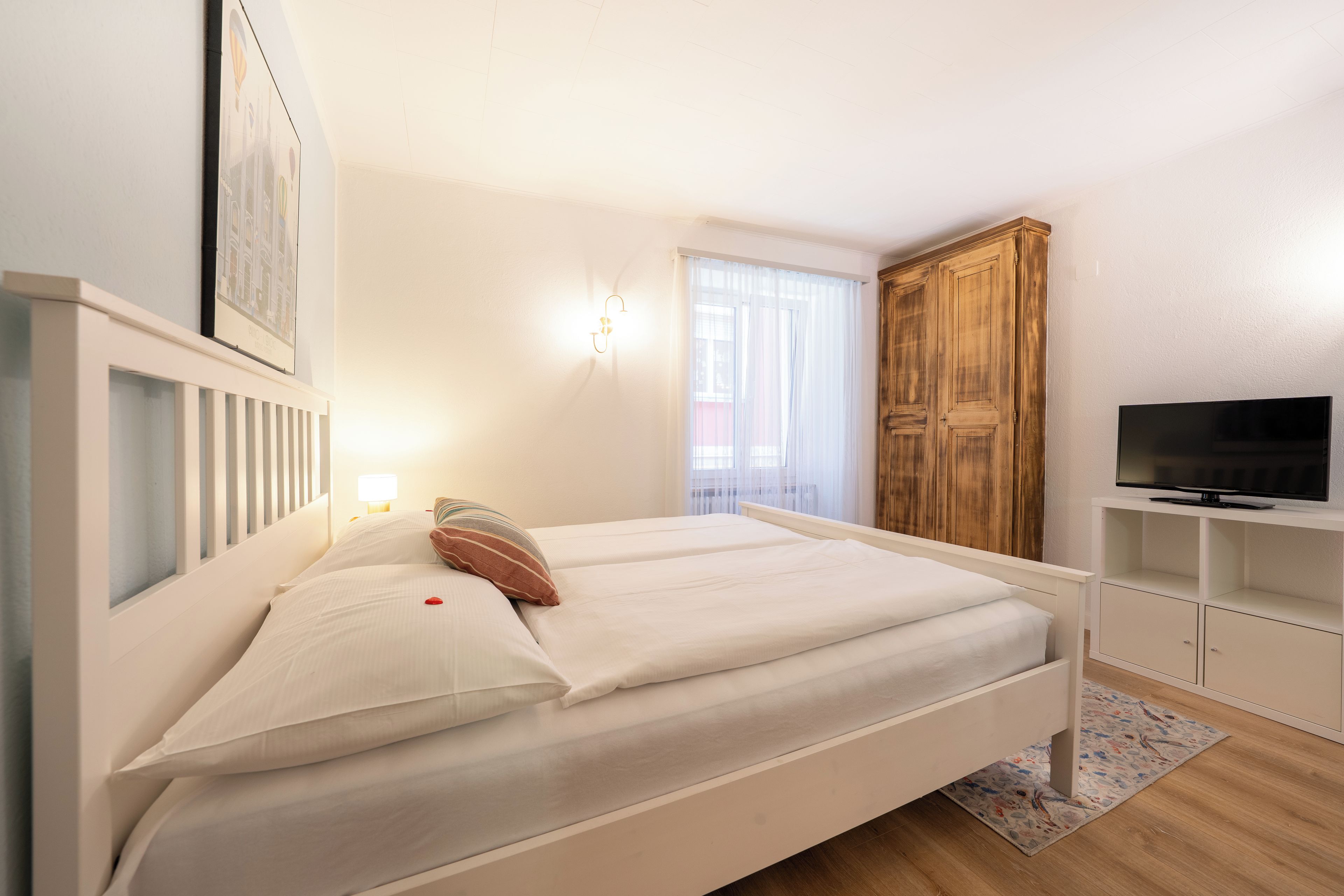 Een slaapkamer met een bed, een televisie, een kledingkast en een raam met gordijnen.