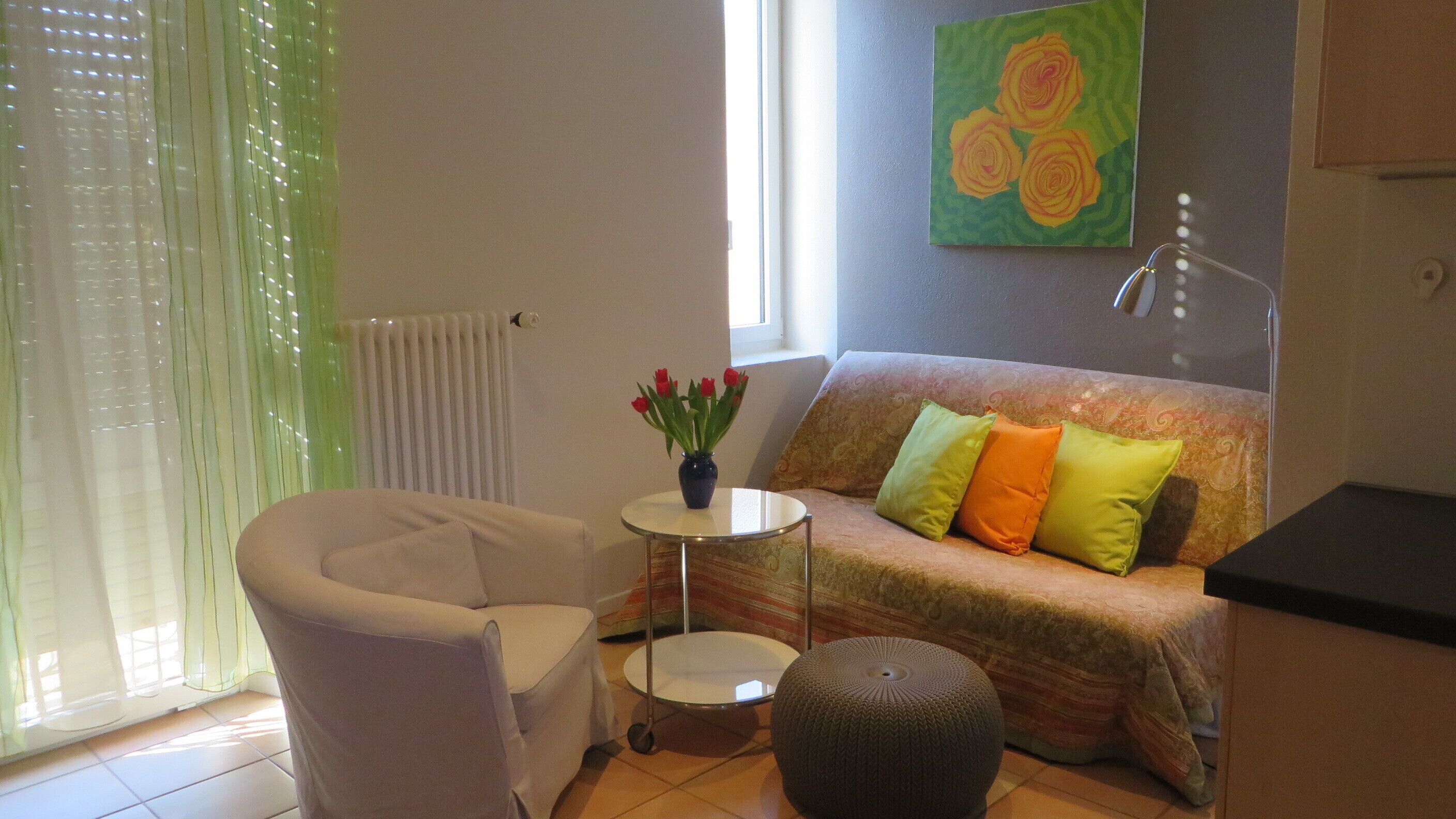 Un salon chaleureux avec un canapé, une petite table ronde, un fauteuil et un vase rempli de fleurs rouges.