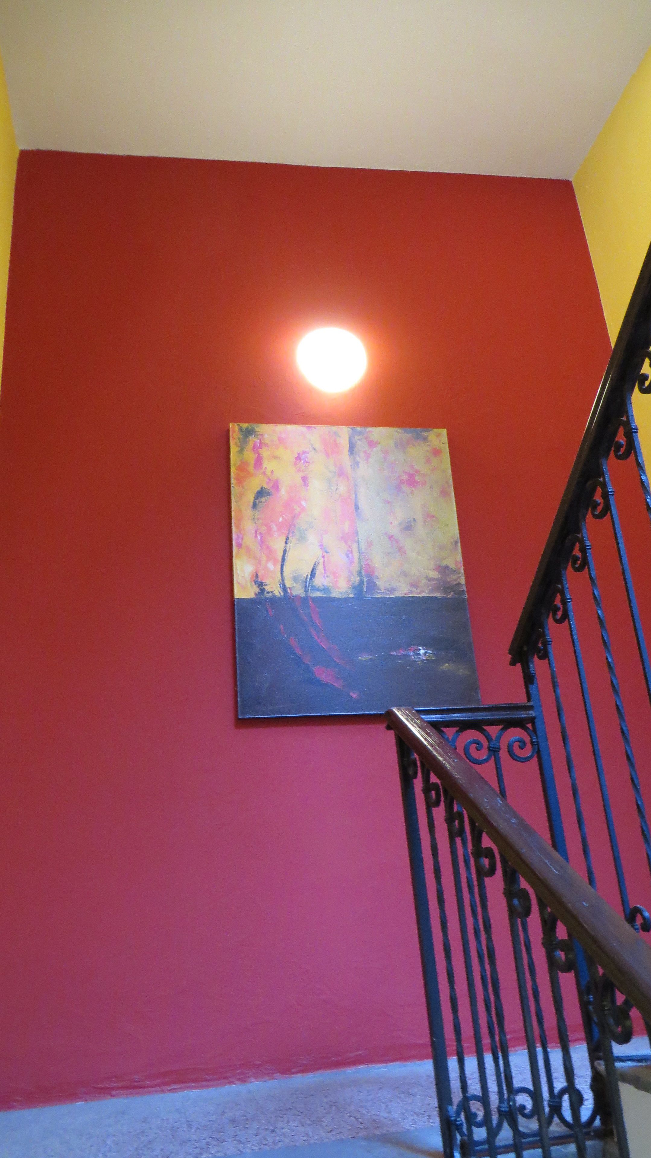 A staircase with a red wall and a painting of a sunset.