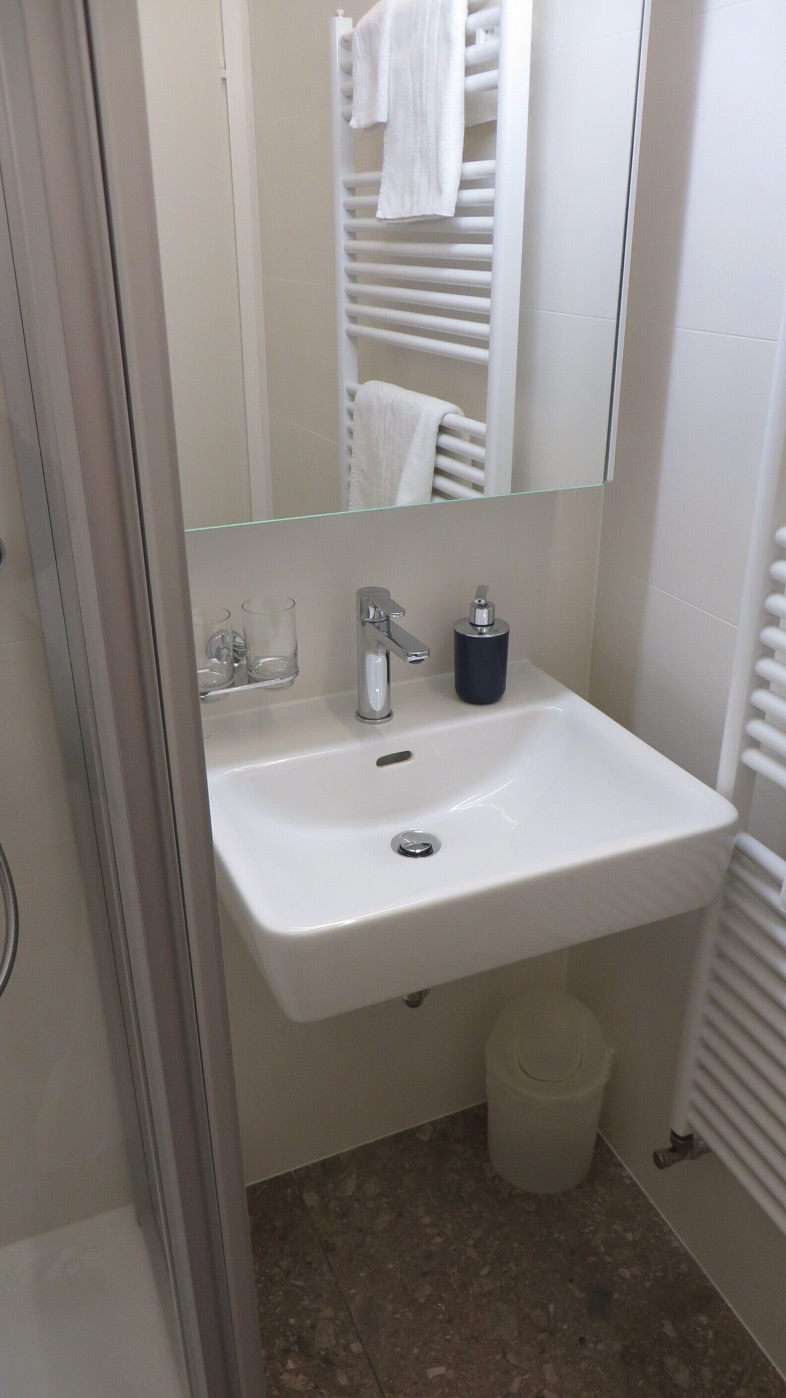 Un bagno con lavandino bianco, uno specchio, un porta asciugamani e un cestino.