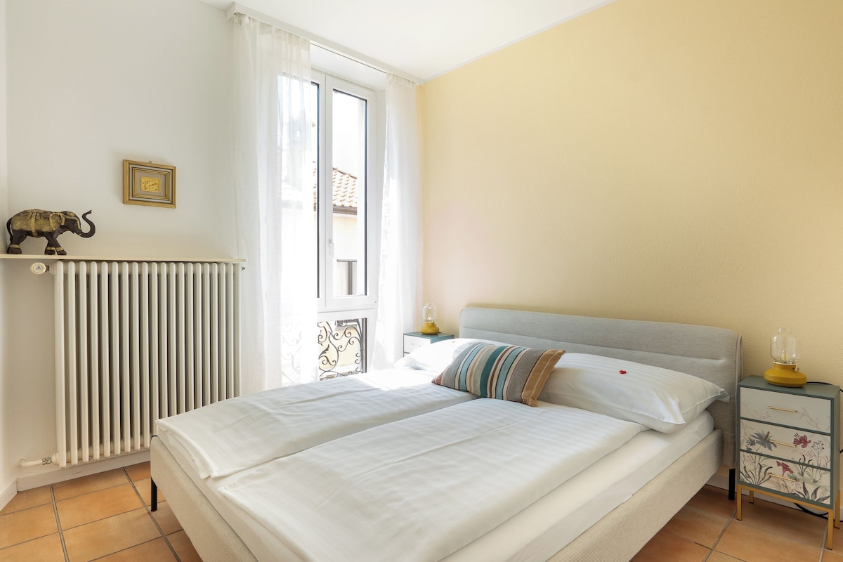 A double bed with white linens, a nightstand with a lamp, and a decorative elephant figurine on the wall.