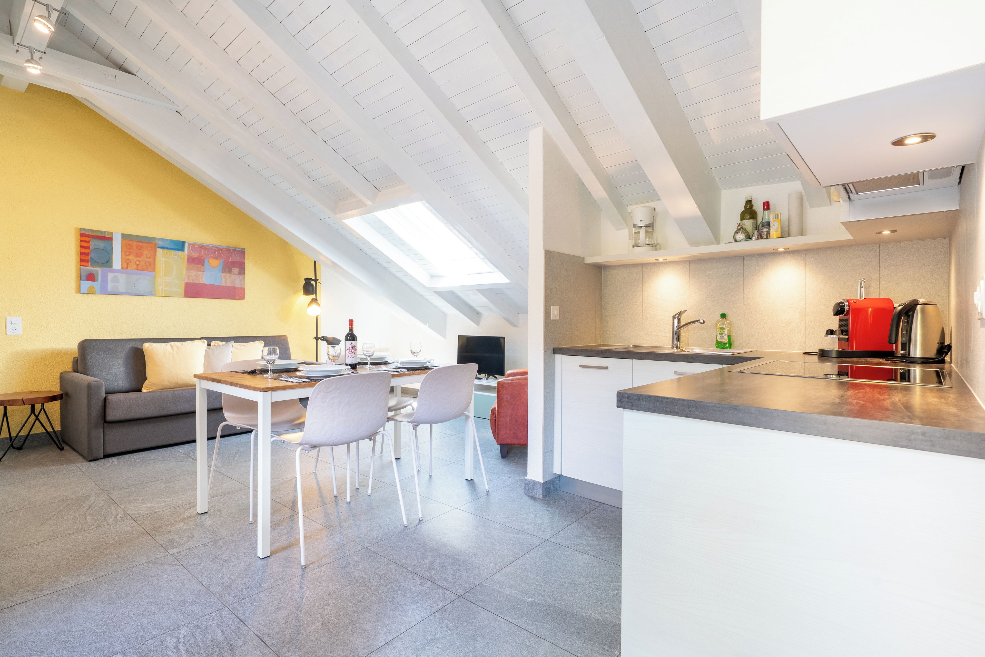 A modern kitchen with a dining area, a sofa, and a TV.
