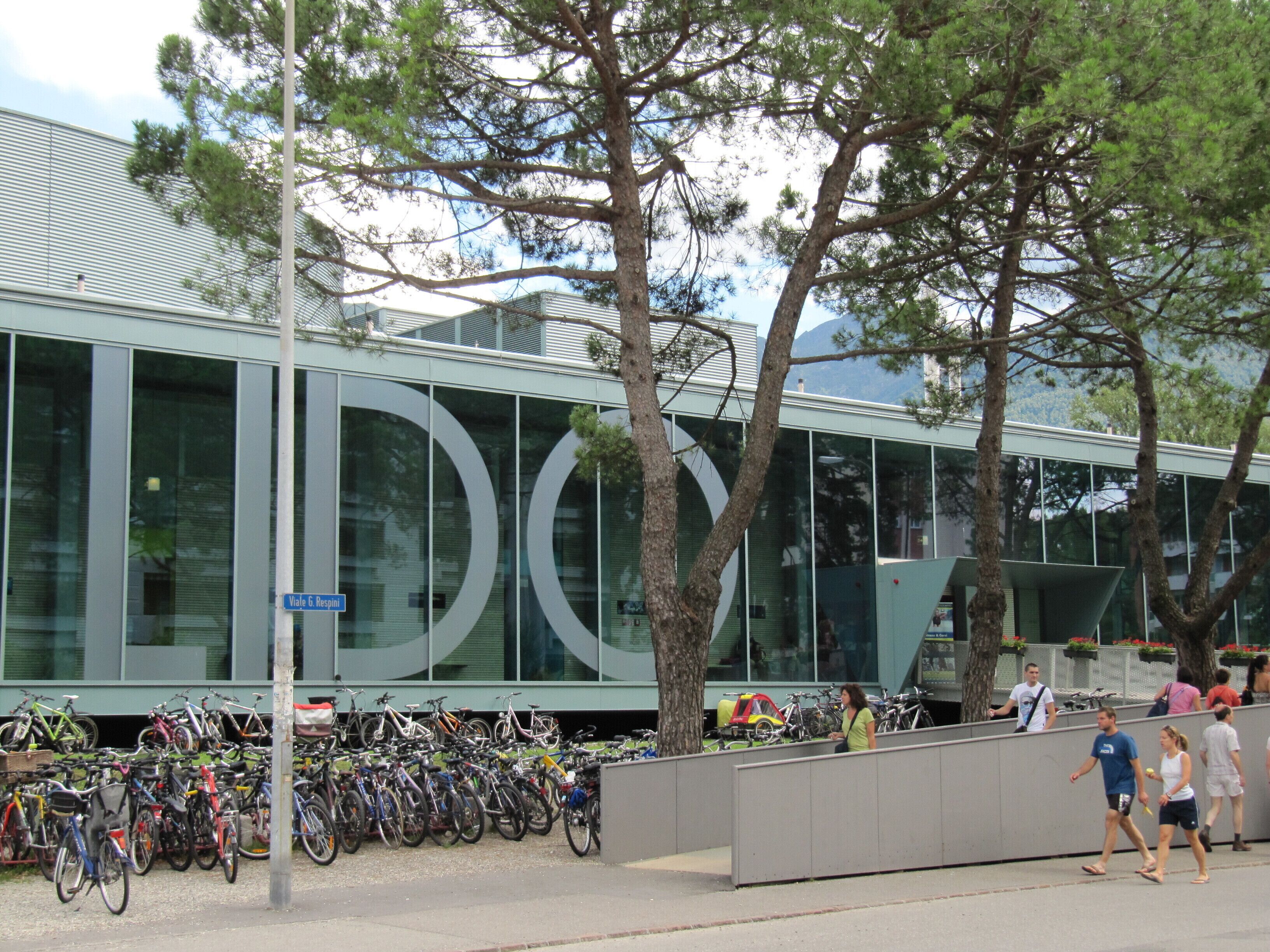 A modern building with a glass facade, a bike parking area, and a pedestrian walkway.