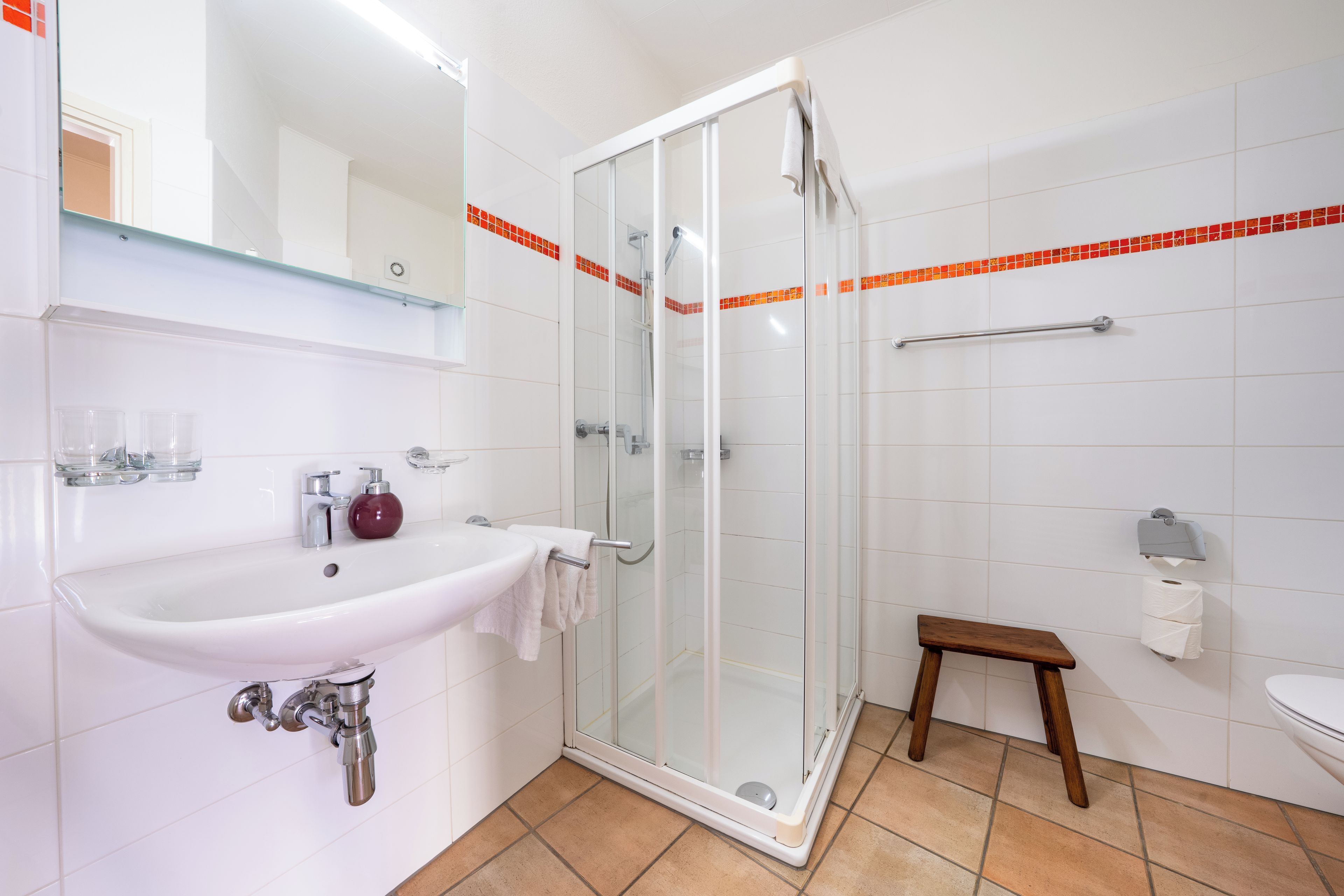 Een badkamer met een douchecabine van glas, een wastafel met een marmeren kom en een klein houten krukje.