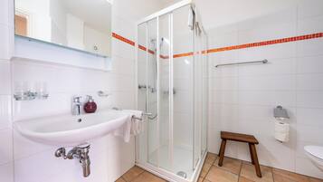 Een badkamer met een douchecabine van glas, een wastafel met een marmeren kom en een klein houten krukje.