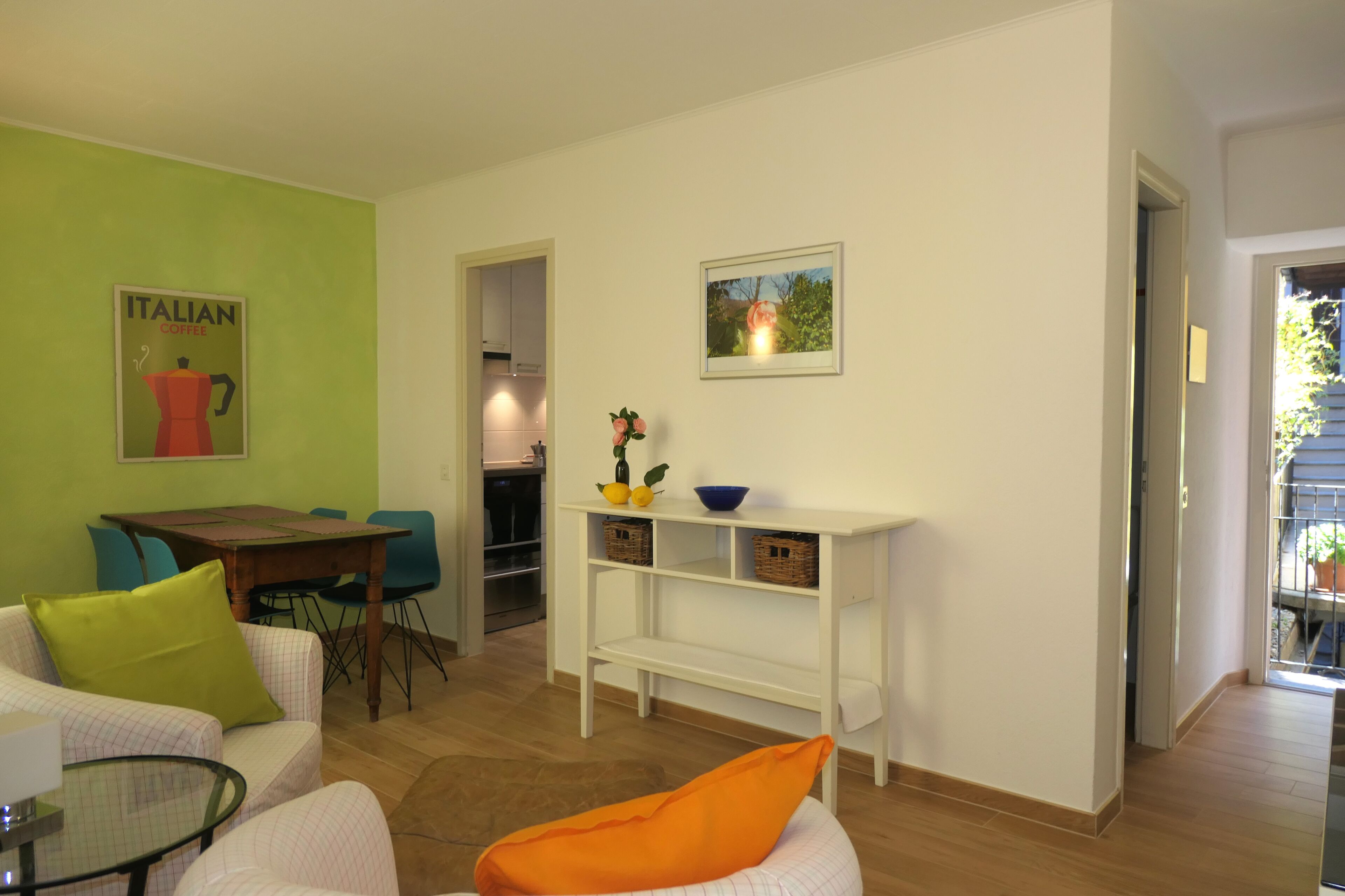 A living room with a green wall, a table, chairs, a sofa, a glass coffee table, and a bookshelf with decorative items.
