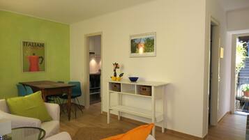 A living room with a green wall, a table, chairs, a sofa, a glass coffee table, and a bookshelf with decorative items.