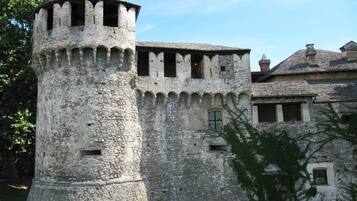 Una torre de pedra històrica amb merlets, part d'un edifici més gran amb teulada de teules.