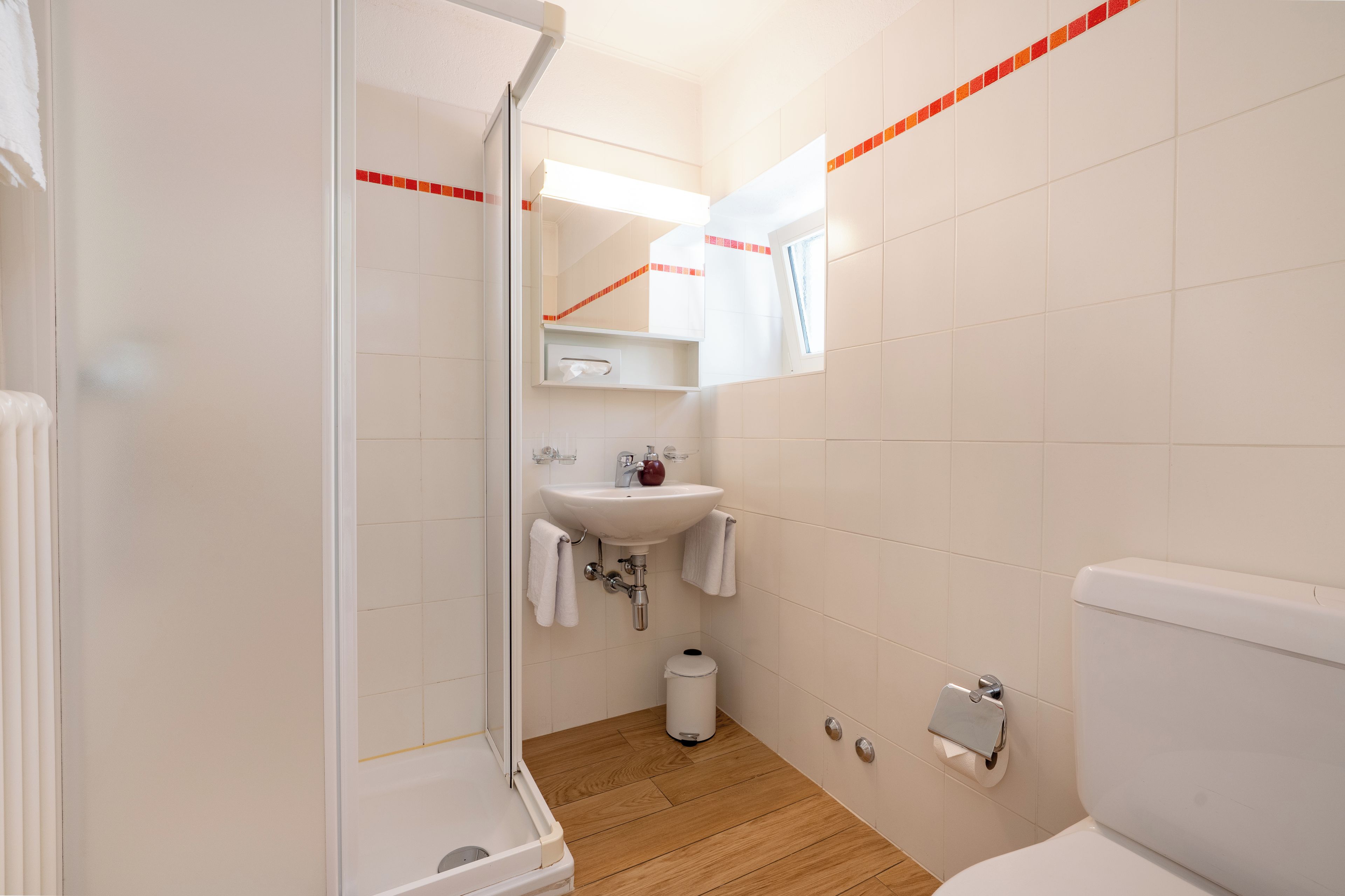 A bathroom with a shower, sink, toilet, and a mirror.