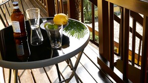 Una mesa redonda con una botella, un vaso y un limón en un balcón con barandas de madera y vistas a un edificio rojo.