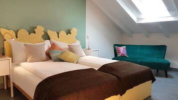 A bedroom with a bed, pillows, a nightstand, a desk, a desk lamp, a green sofa, and a skylight.
