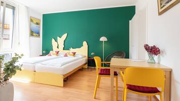 Una habitación con cama, escritorio, silla, lámpara y un jarrón con flores.