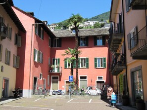 A multi-story building with a red facade, green shutters, and a central courtyard with a palm tree.