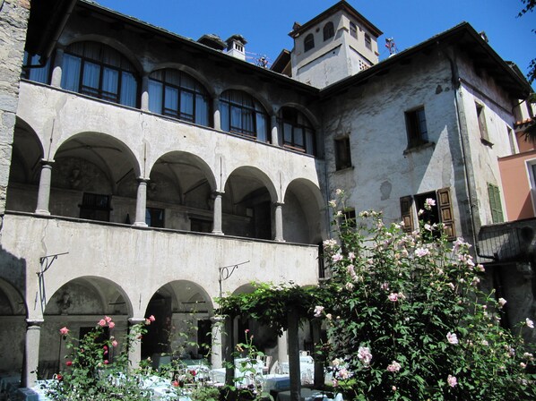 A historic building with multiple arches and a courtyard with blooming flowers.
