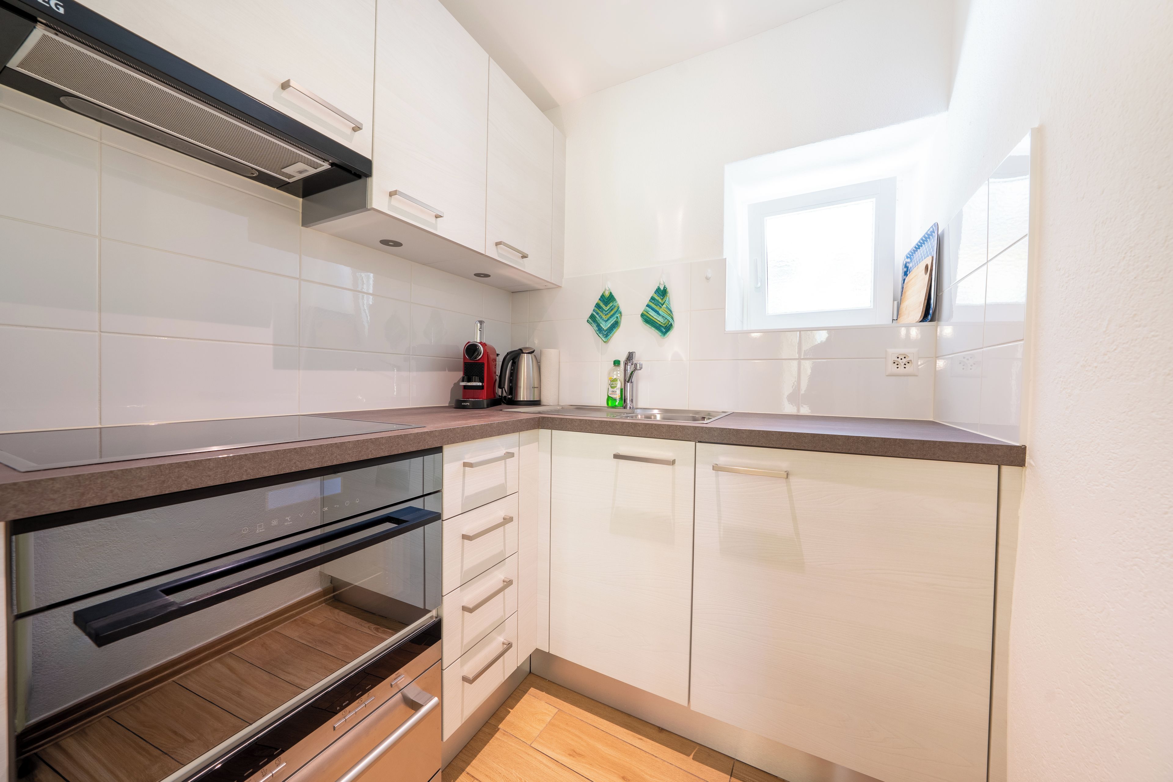 A modern kitchen with white cabinetry, a built-in oven, and a window above the sink.