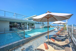 Zona junto a la piscina con sillones de descanso y sombrillas, un bar y una piscina cubierta con cristal.