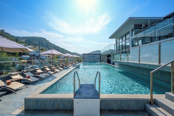 Una piscina con sillas de sol y sombrillas, rodeada de edificios y colinas.