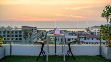A balcony with two chairs and a table, overlooking a cityscape at sunset.
