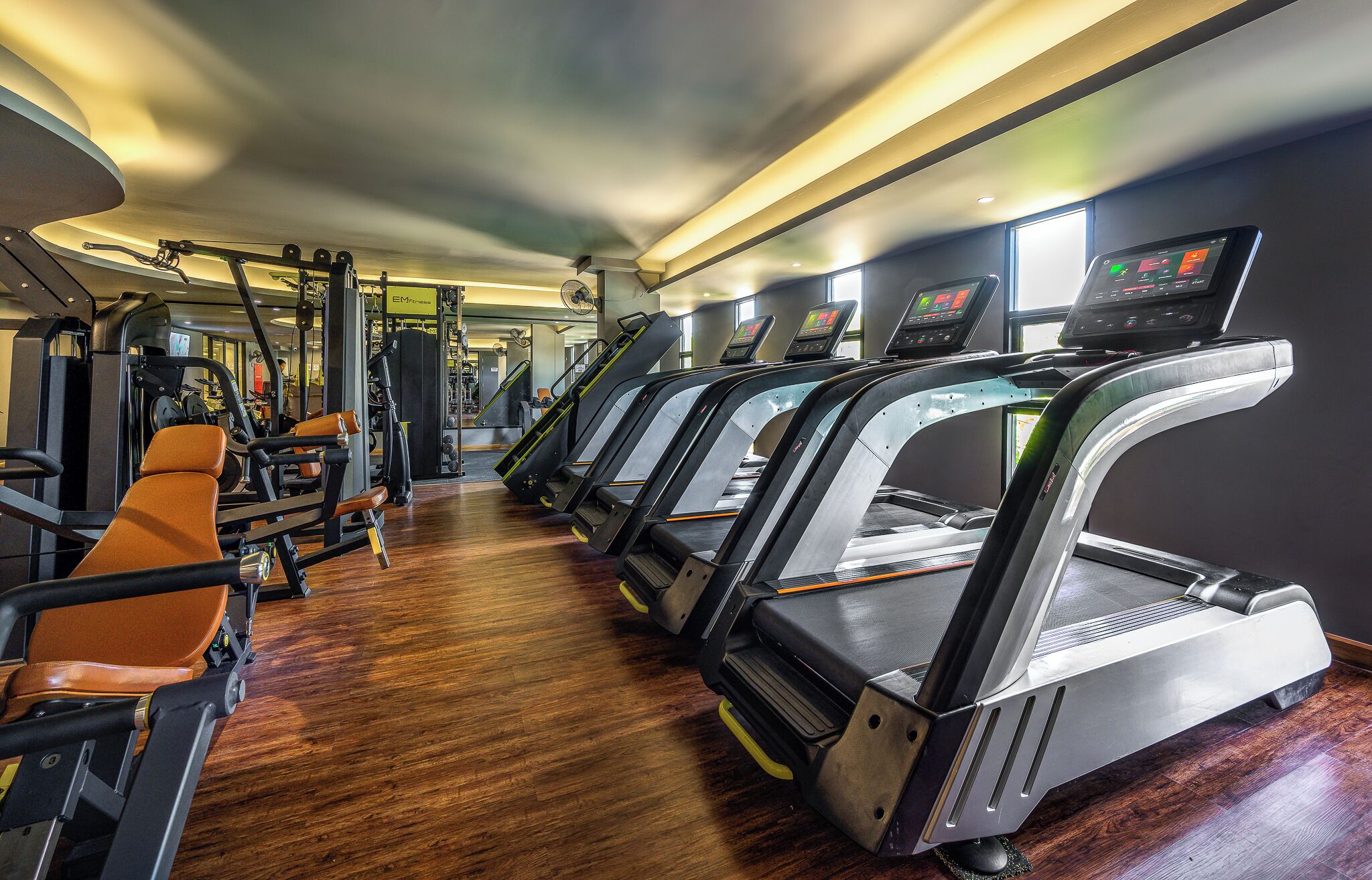Une salle de sport équipée de tapis de course, d’appareils de musculation et dotée d’un plancher en bois.